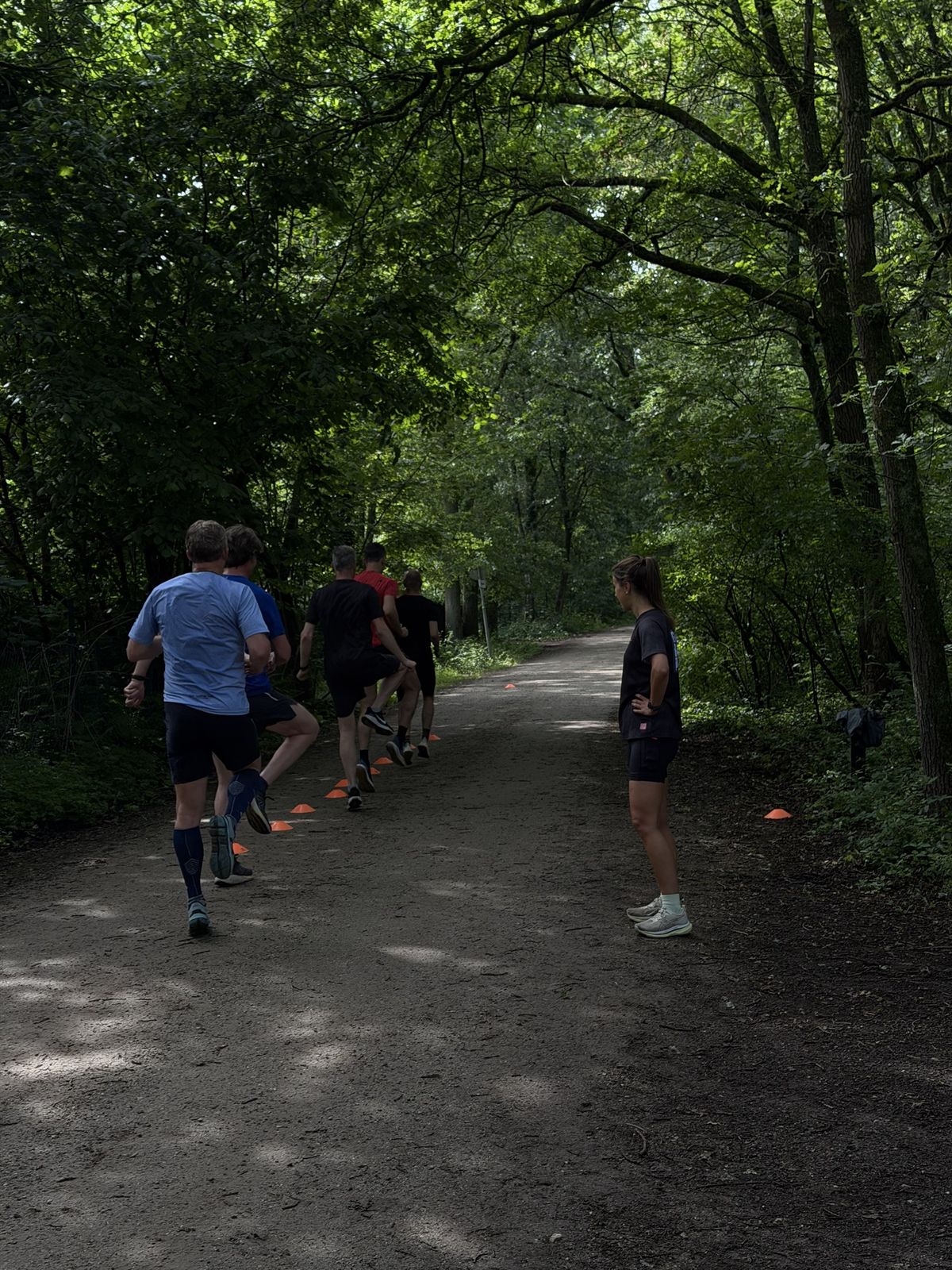Group of runners doing drills along cones while a coach watches